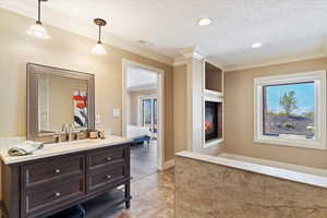 Bathroom featuring visible vents, connected bathroom, a glass covered fireplace, crown molding, and a textured ceiling