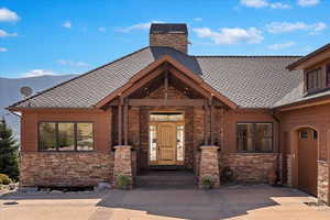 Property entrance with stone siding, roof with shingles, and a chimney