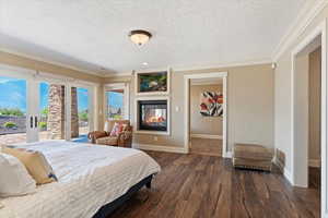 Bedroom with ornamental molding, dark wood-type flooring, a multi sided fireplace, and access to exterior