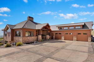 View of front facade with metal roof, a garage, concrete driveway, stone siding, and a standing seam roof