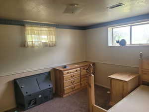 Carpeted bedroom with a wainscoted wall, a textured ceiling, visible vents, and wallpapered walls