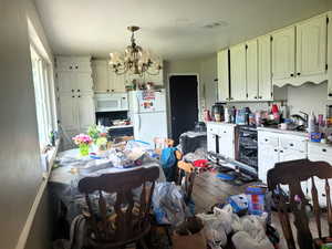 Kitchen featuring white appliances, hanging light fixtures, a notable chandelier, light countertops, and a sink