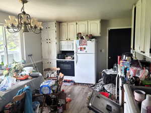 Kitchen with white appliances, white cabinets, an inviting chandelier, and wood finished floors