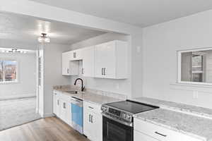 Kitchen featuring light stone counters, stainless steel electric stove, white cabinets, a sink, and dishwashing machine