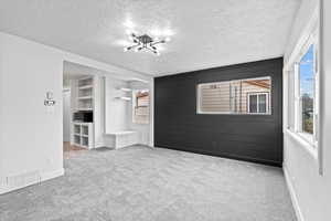 Carpeted spare room featuring visible vents, a textured ceiling, and baseboards