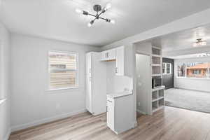 Kitchen featuring baseboards, light wood-style flooring, white cabinetry, and a textured ceiling