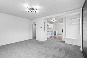 Unfurnished living room with a textured ceiling, carpet, and baseboards