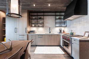 Kitchen featuring wall chimney range hood, premium stove, dark wood-type flooring, and a sink