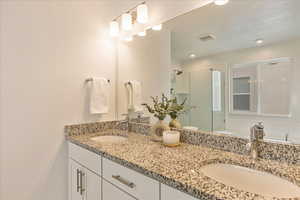 Bathroom featuring double vanity, a stall shower, visible vents, and a sink