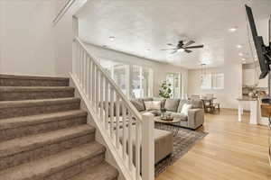 Living room with baseboards, ceiling fan, stairs, a textured ceiling, and light wood-type flooring