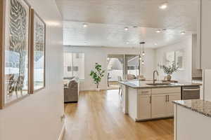 Kitchen with open floor plan, a sink, light stone countertops, light wood-type flooring, and dishwasher