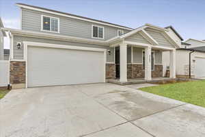 View of front facade with a garage, concrete driveway, a porch, and stone siding