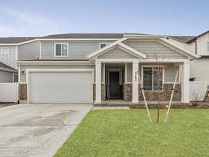 Craftsman house with a porch, concrete driveway, fence, stone siding, and a front lawn