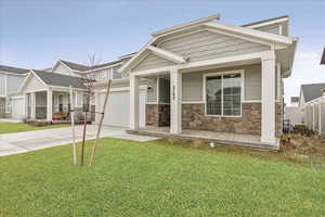 Craftsman-style home featuring an attached garage, covered porch, driveway, stone siding, and a front yard