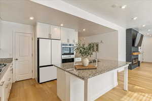 Kitchen with light stone counters, a sink, freestanding refrigerator, and light wood-style floors