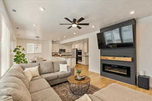 Living room featuring recessed lighting, visible vents, a glass covered fireplace, a textured ceiling, and light wood-type flooring