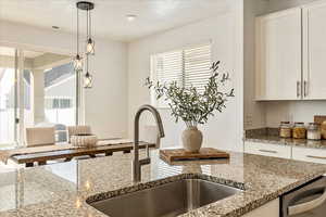 Kitchen with hanging light fixtures, light stone countertops, and a sink