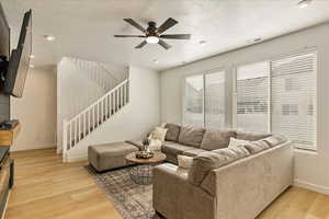 Living area with baseboards, a ceiling fan, stairs, a textured ceiling, and light wood-style floors