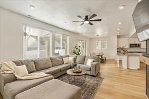 Living room featuring baseboards, visible vents, light wood-style flooring, ceiling fan, and a textured ceiling