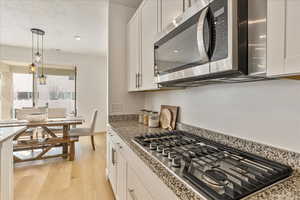 Kitchen featuring hanging light fixtures, appliances with stainless steel finishes, white cabinets, and light wood-style floors