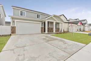 View of front of house with concrete driveway, stone siding, a front yard, and fence