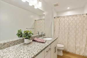 Full bathroom with toilet, wood finished floors, visible vents, vanity, and a shower with curtain