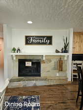 Room details featuring a stone fireplace, a textured ceiling, and wood finished floors