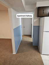 Corridor featuring a wainscoted wall, light carpet, and a textured ceiling