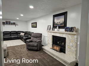 Living room featuring carpet floors, recessed lighting, a stone fireplace, and a textured ceiling