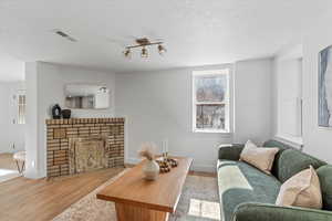 Living room with a textured ceiling, a brick fireplace, wood finished floors, and visible vents