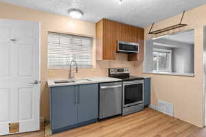 Kitchen featuring light countertops, visible vents, a textured wall, appliances with stainless steel finishes, and light wood-type flooring