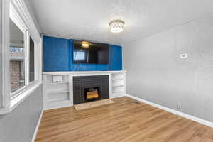 Unfurnished living room featuring a textured ceiling, a textured wall, a fireplace, wood finished floors, and visible vents