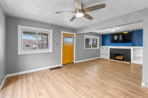 Unfurnished living room featuring baseboards, visible vents, wood finished floors, a textured ceiling, and a brick fireplace