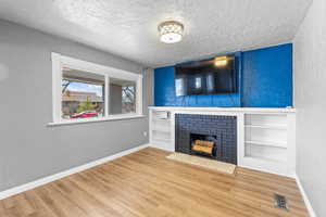 Unfurnished living room featuring a textured ceiling, a textured wall, a fireplace, wood finished floors, and visible vents