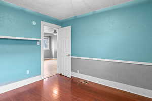 Spare room featuring baseboards, visible vents, a textured wall, wood finished floors, and a textured ceiling