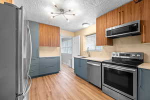 Kitchen with light wood finished floors, appliances with stainless steel finishes, light countertops, a textured ceiling, and a sink