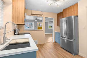 Kitchen with visible vents, freestanding refrigerator, light countertops, light wood-type flooring, and a sink