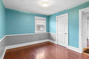 Unfurnished bedroom with a textured ceiling, a textured wall, wood finished floors, and baseboards