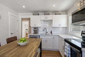 Kitchen featuring white cabinets, decorative backsplash, stainless steel appliances, wooden counters, and a sink