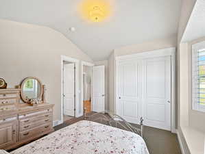Bedroom featuring visible vents, baseboards, a closet, lofted ceiling, and dark carpet