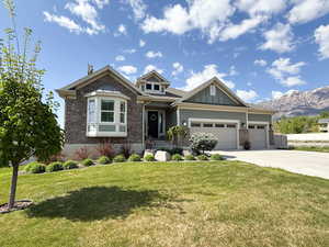 Craftsman house featuring an attached garage, stone siding, a front yard, a mountain view, and concrete driveway