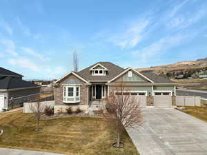 Craftsman house with a front yard, fence, a garage, stone siding, and driveway