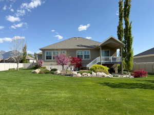 Rear view of house featuring a shingled roof, stucco siding, a yard, and fence