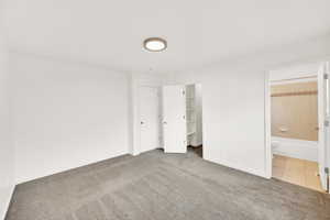 Unfurnished bedroom with tile patterned flooring, connected bathroom, carpet floors, baseboards, and a walk in closet