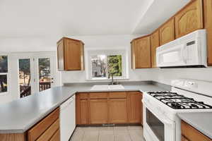 Kitchen featuring white appliances, light tile patterned floors, visible vents, a peninsula, and a sink