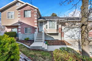 Tri-level home with driveway, brick siding, an attached garage, and stucco siding