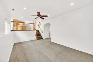 Carpeted empty room with stairs, visible vents, arched walkways, and recessed lighting