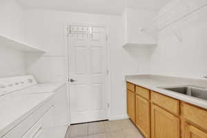 Laundry room featuring cabinet space, light tile patterned flooring, independent washer and dryer, and a sink