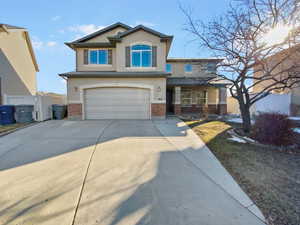 View of front of property featuring concrete driveway, brick siding, fence, and stucco siding