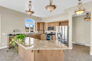Kitchen featuring light stone counters, pendant lighting, stainless steel appliances, visible vents, and a sink